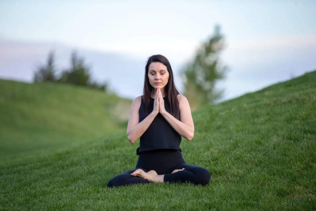woman meditating outdoors on grass hill